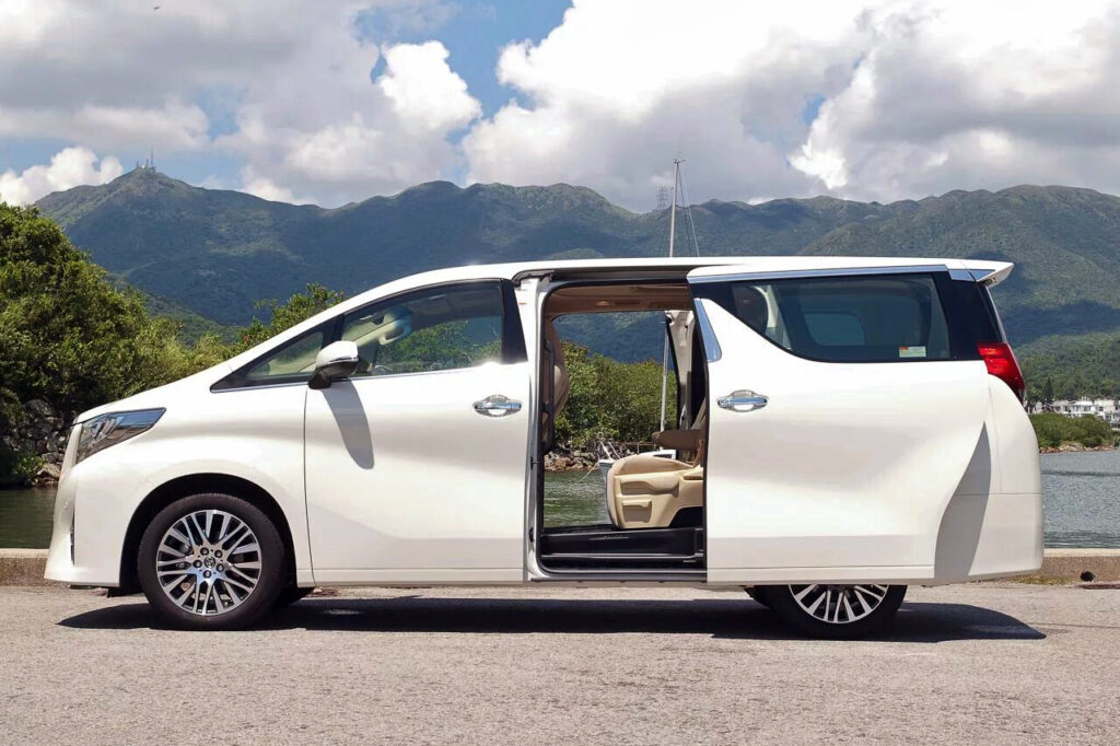 Mobil Toyota Alphard mewah sedang berjalan di jalanan Bali pada malam hari, Alt text: Sewa Alphard di Bali malam har